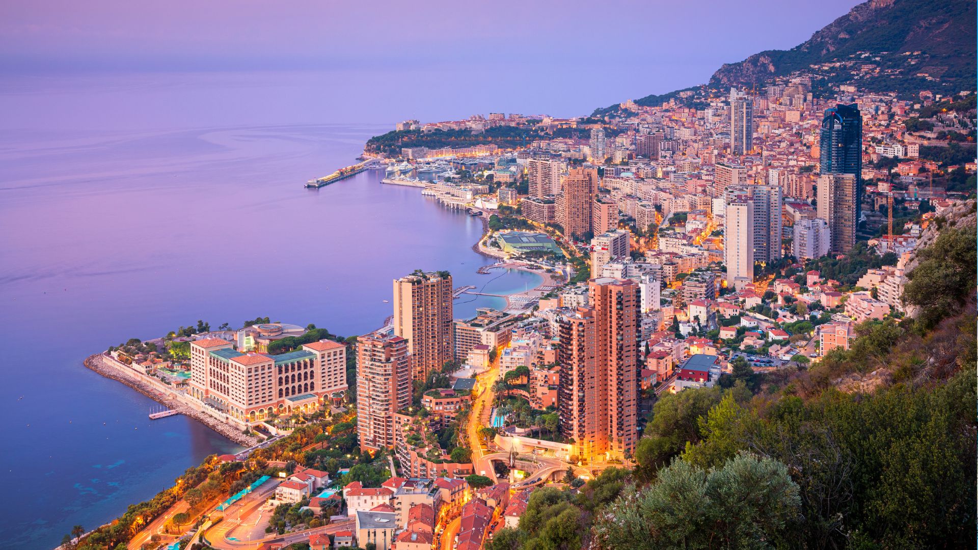 Monaco's skyline and coastline at dusk above the harbor.