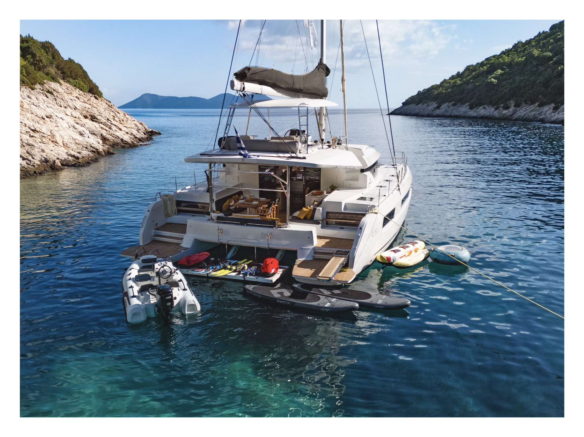 Crewed catamaran at anchor with paddleboards and water toys deployed off the stern